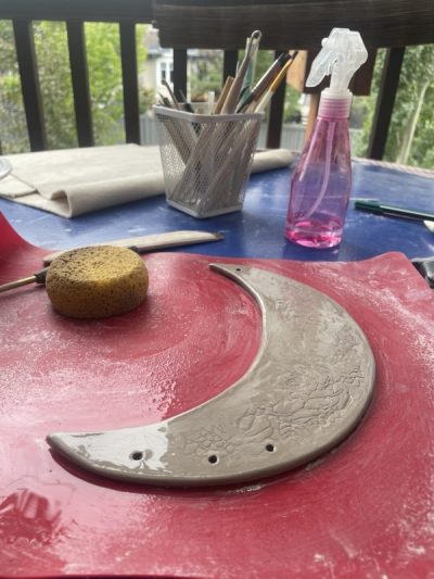 a tabletop workspace with a clay crescent moon in progress, with  clay tools in the background